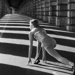 Woman stretching under urban bridge in monochrome capturing dynamic sport pose.